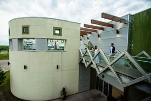 Modern architectural building with curved walls and geometric glass roof features against cloudy sky.
