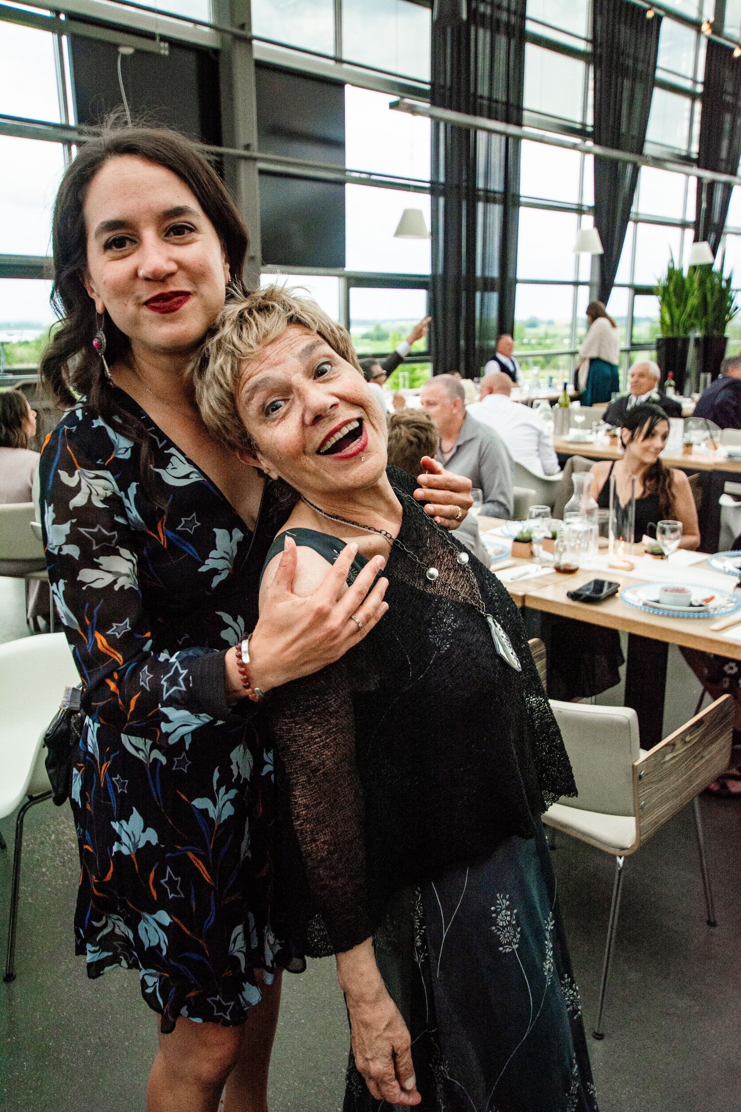 Two people share a playful moment while dining at a modern restaurant with large windows.