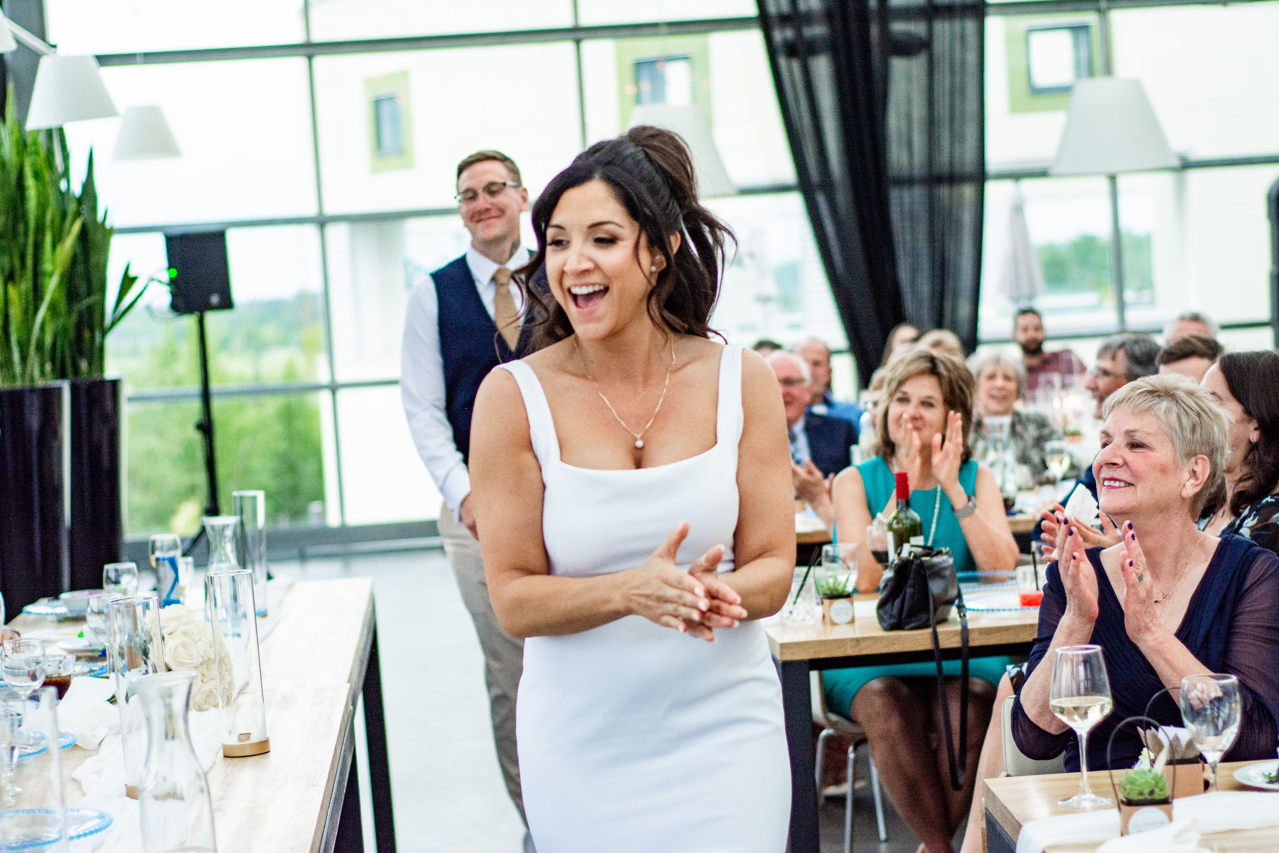Wedding guests raise champagne glasses during a joyful reception celebration in a bright modern venue.