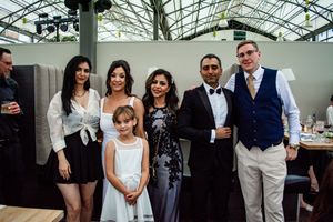 Wedding party celebrates with champagne and laughter in a bright indoor venue with glass ceiling.