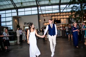 Wedding reception guests dancing and celebrating in a modern venue with large glass windows and natural light.