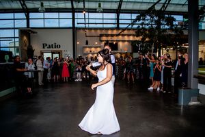 Wedding guests dance and celebrate on a spacious dance floor at an indoor reception venue.