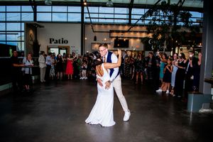 Wedding celebration with dancing couples under large glass atrium and string lights.