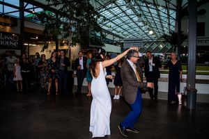 Wedding guests dancing in spacious venue with glass ceiling and natural lighting.