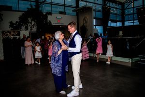 Wedding guests dance together on a dark dance floor during an evening reception celebration.