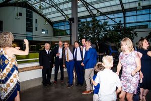 Wedding guests gather under a glass atrium roof during an evening reception at an elegant venue.