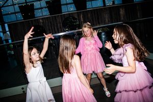 Young children in pink and white dresses dancing together at a celebration event.