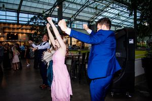 A couple dancing energetically at an indoor reception venue with glass ceiling and festive lighting.