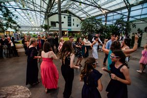 Wedding reception venue with glass ceiling and guests dancing in an elegant greenhouse setting.