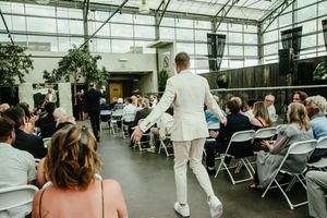 Wedding guests seated in folding chairs inside a modern greenhouse venue.