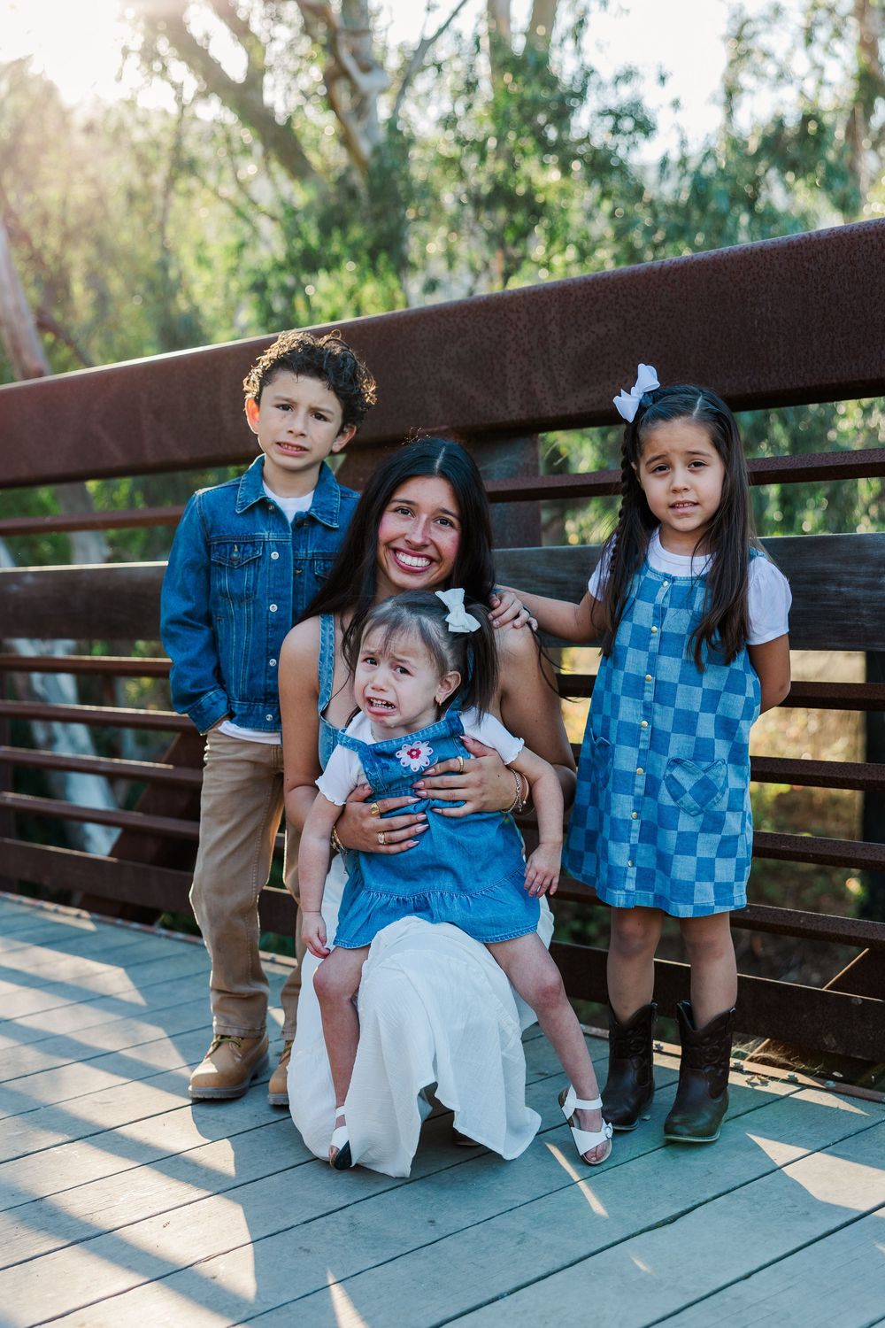 Family members in matching denim outfits pose together on a wooden bridge during a sunny outdoor photoshoot.