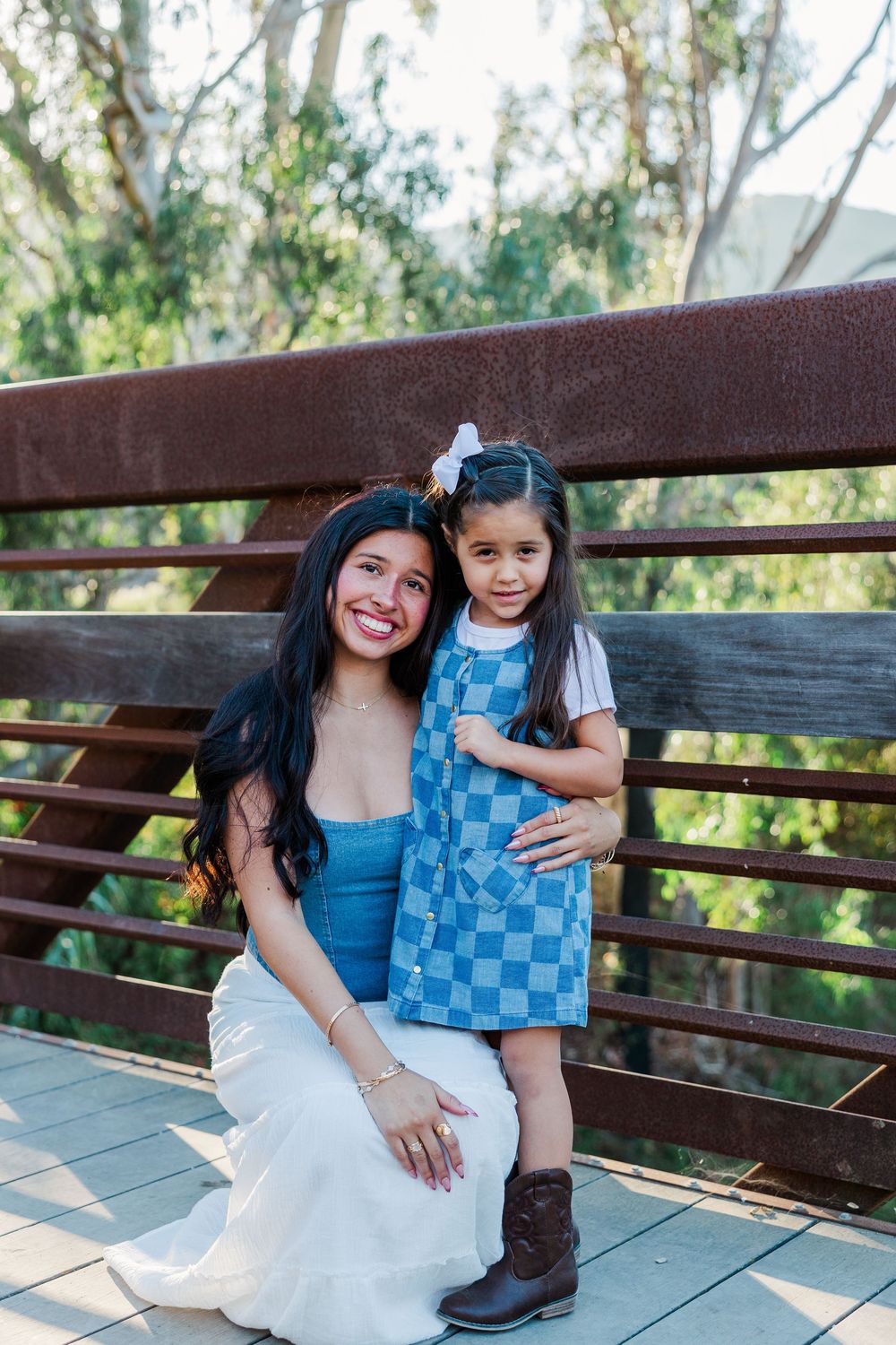 Two people sit together on a wooden bench in a park setting wearing coordinating blue and white outfits.