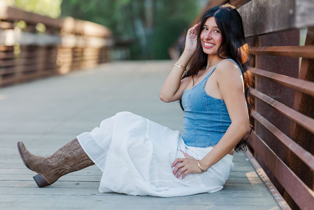 Woman in denim top and white skirt poses on wooden deck during sunset photoshoot.