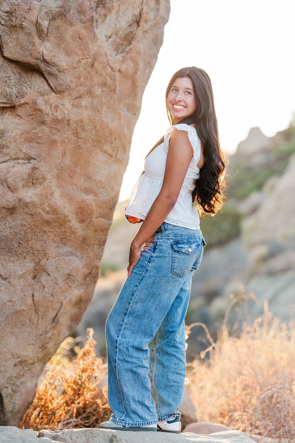 Casual outdoor fashion poses near rocky formations at golden hour wearing denim and white.