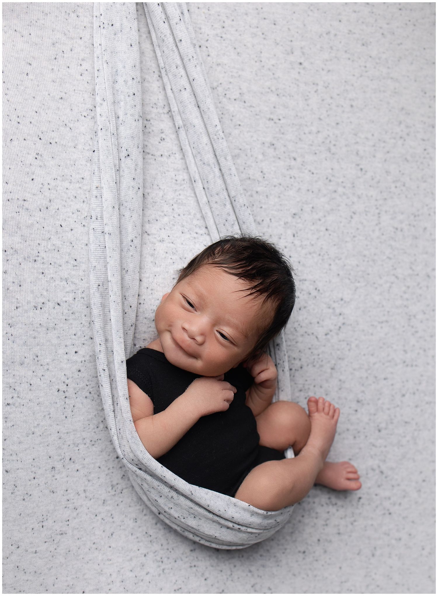 Smiling newborn girl.  swaddled in blue wearing a blue floral headband laying in a bowl with blue curly fur.