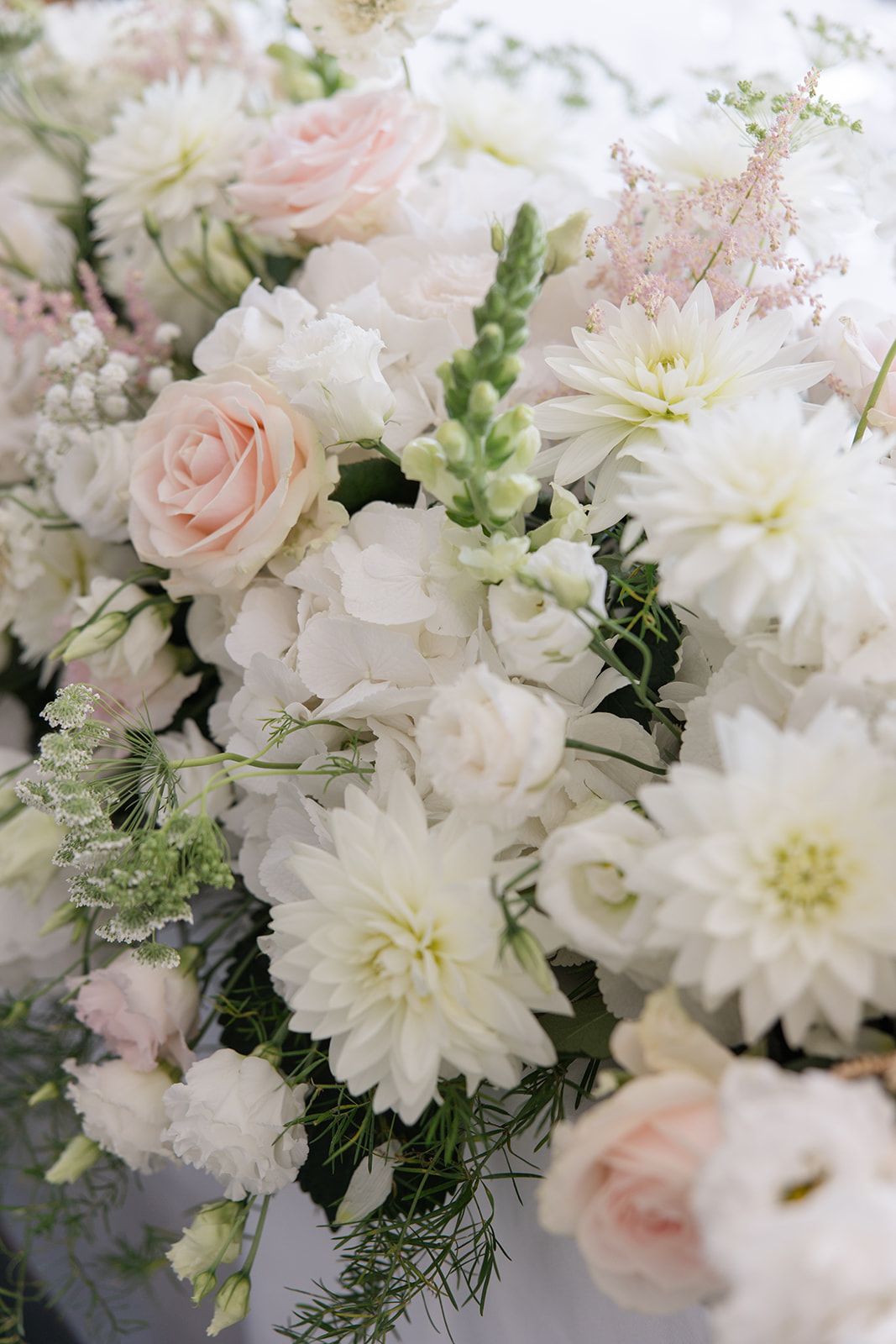 A romantic wedding bouquet featuring soft white dahlias, blush pink roses, and delicate greenery in an elegant arrangement.