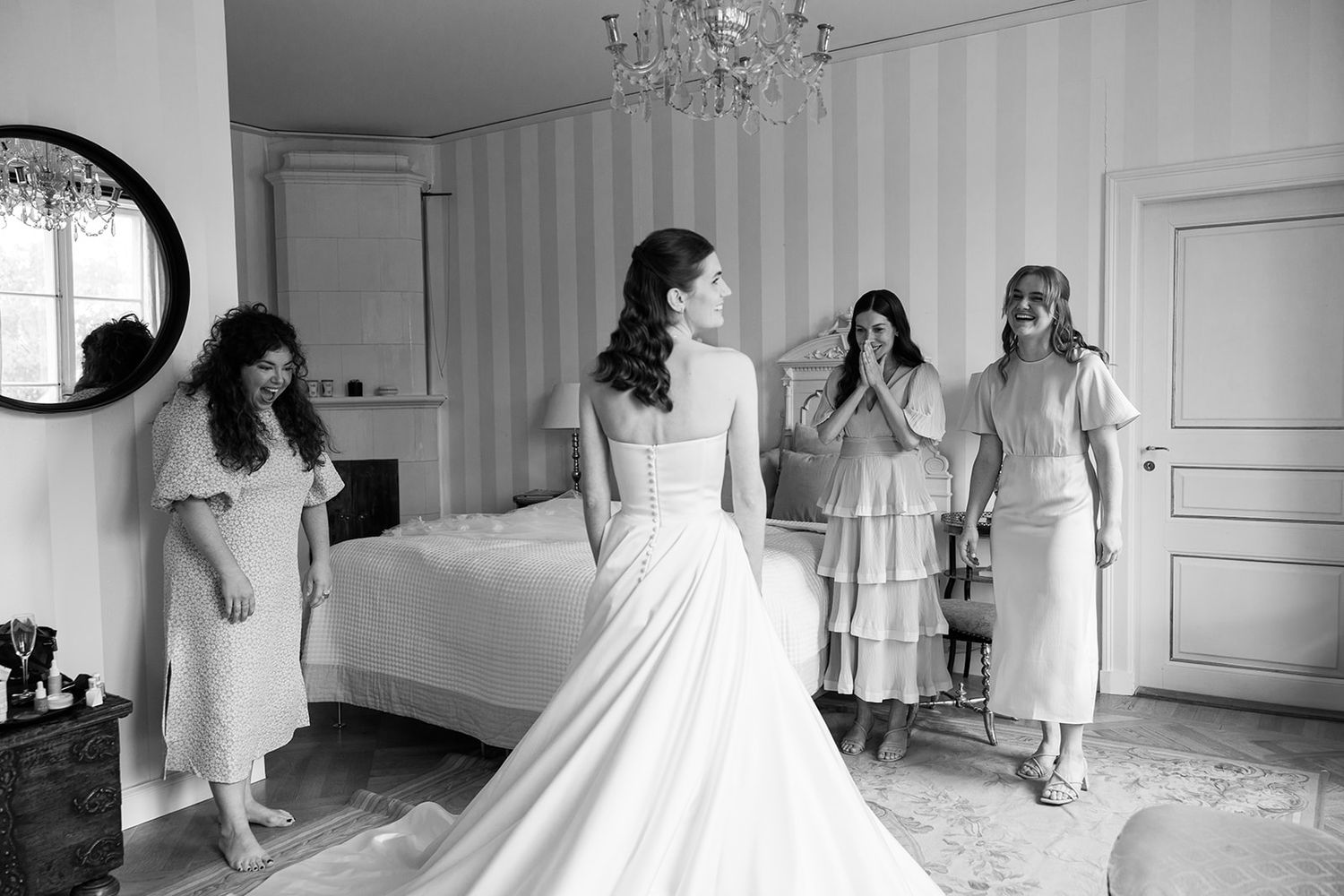 Black and white photo of bridal preparations in an elegant bedroom with a chandelier and round mirror.