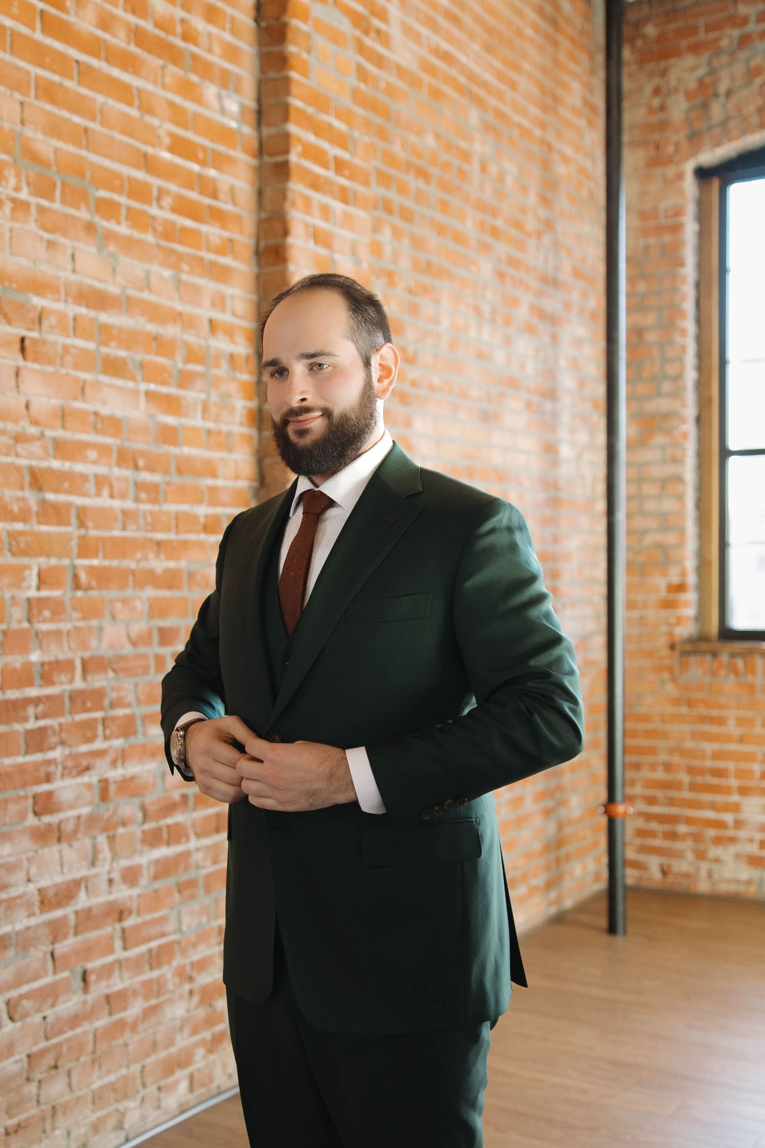 Two men in dark suits gesturing and posing in an industrial brick loft space with hardwood floors.