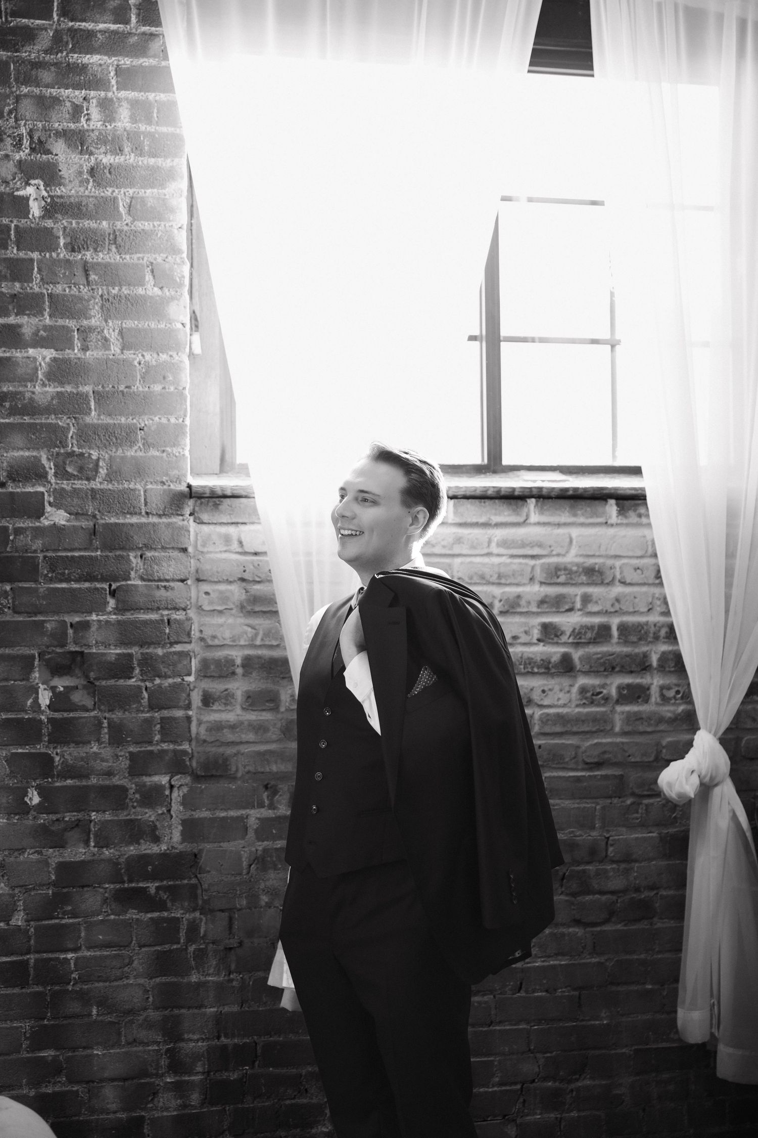 Black and white triptych photograph showing a figure in formal attire against a brick wall with white curtains.