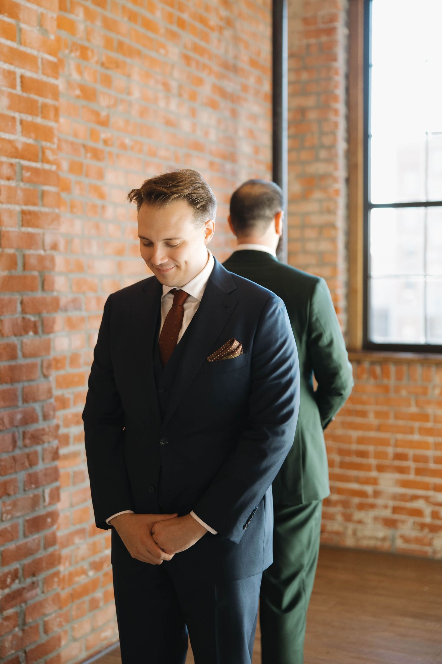 Business professionals in suits stand thoughtfully in an industrial-style office space with exposed brick walls.
