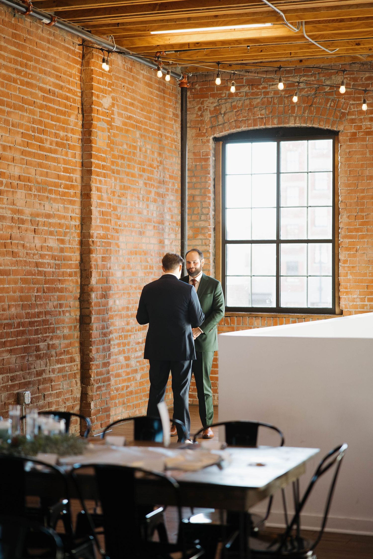 A rustic industrial event space with exposed brick walls, wooden beams, and string lights.
