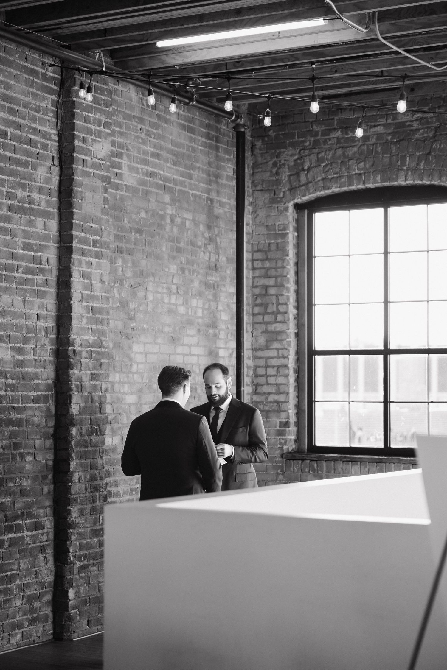 A series of black and white photos showing a couple in an industrial loft space with exposed brick walls and windows.