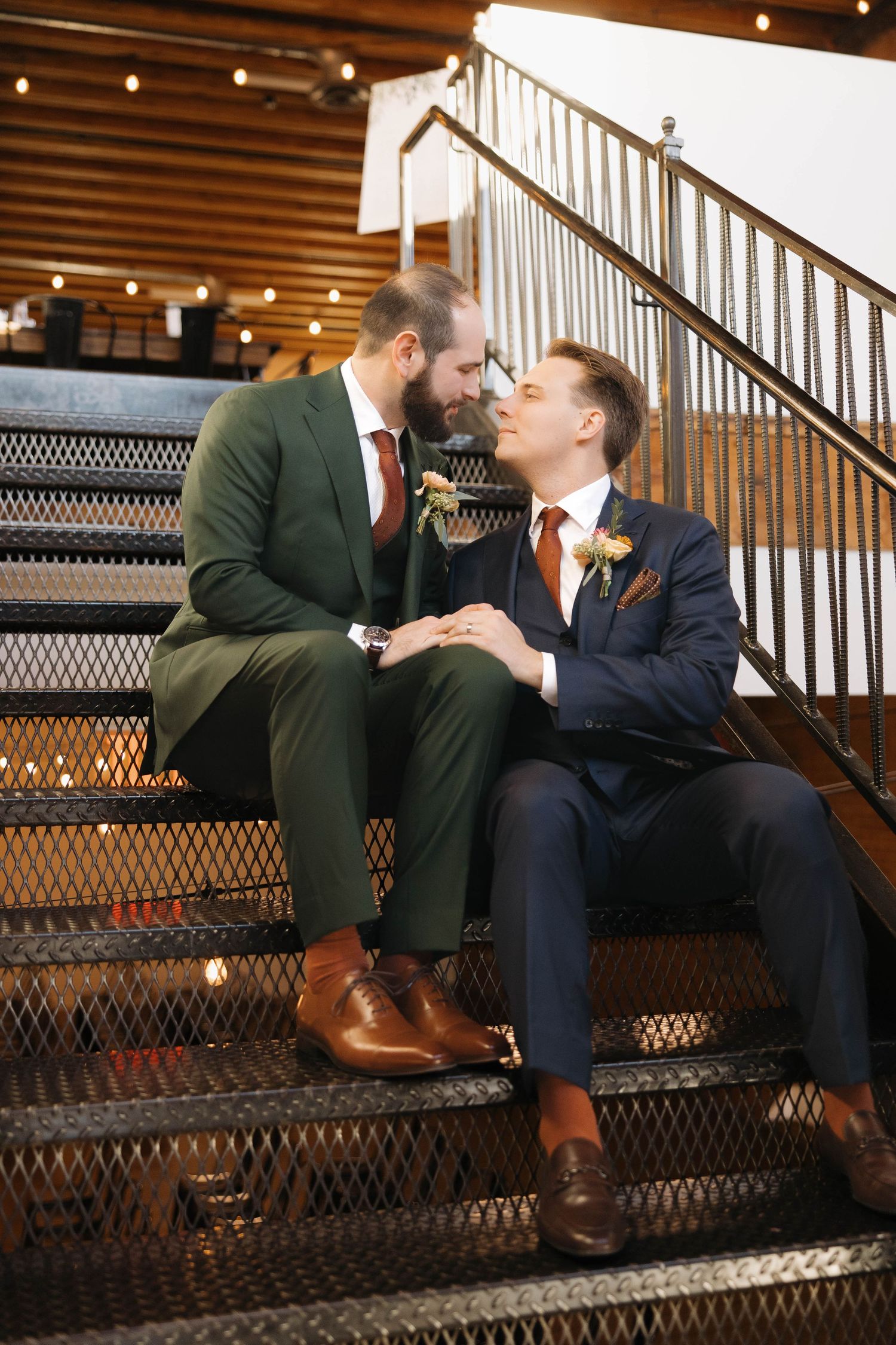A couple sitting on wooden stairs shares an intimate moment in a warmly lit indoor setting.