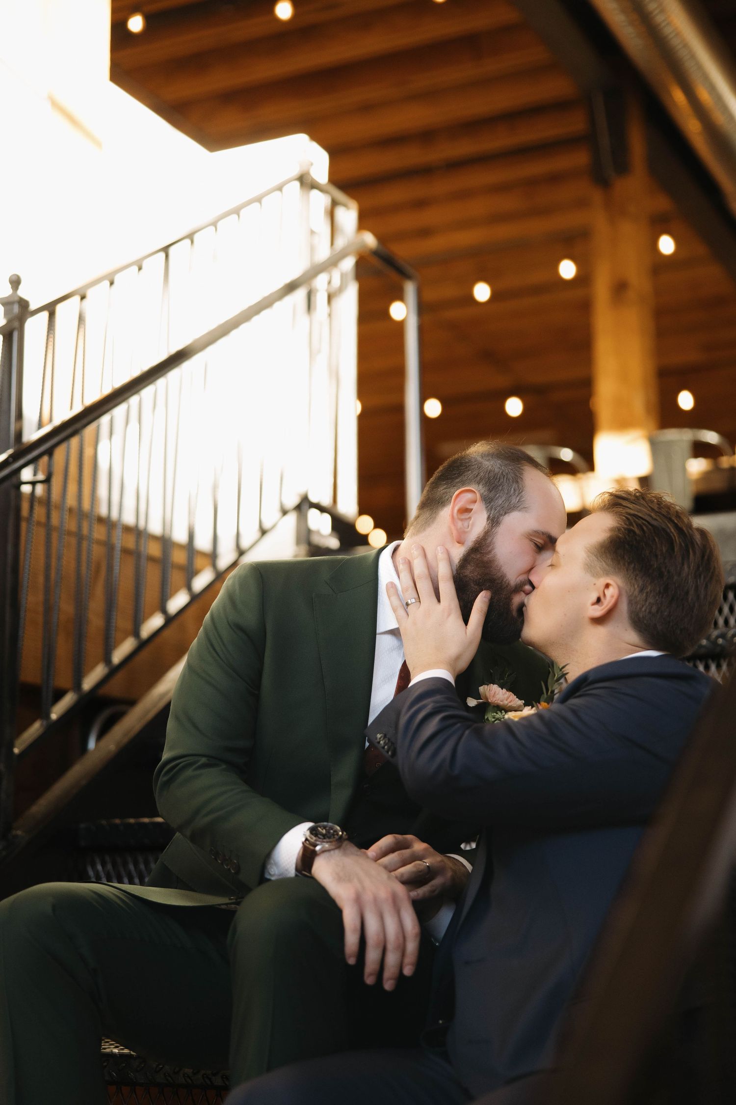 A romantic couple sharing intimate moments on a couch in a warmly lit indoor setting with wooden stairs.