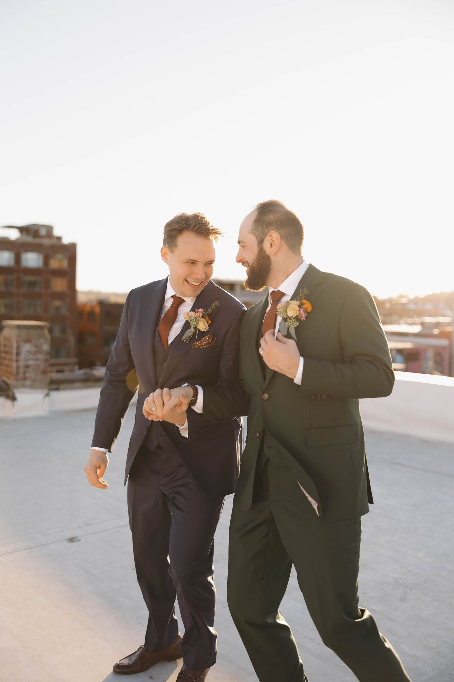 Playful candid moment between two people in suits dancing on an urban rooftop at sunset.