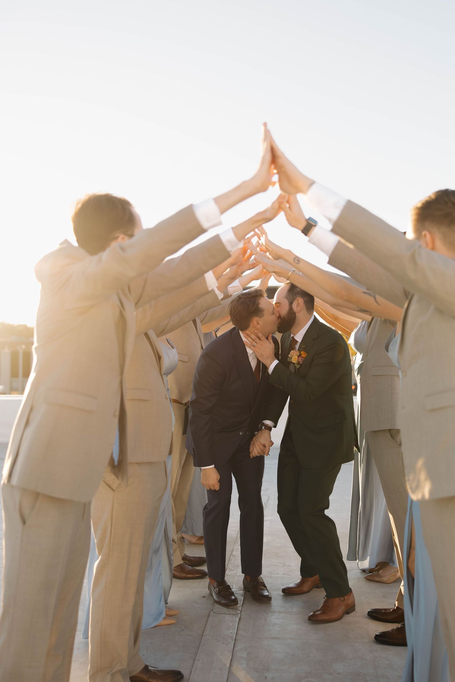 Wedding party forms a tunnel with raised arms on a rooftop during golden hour.