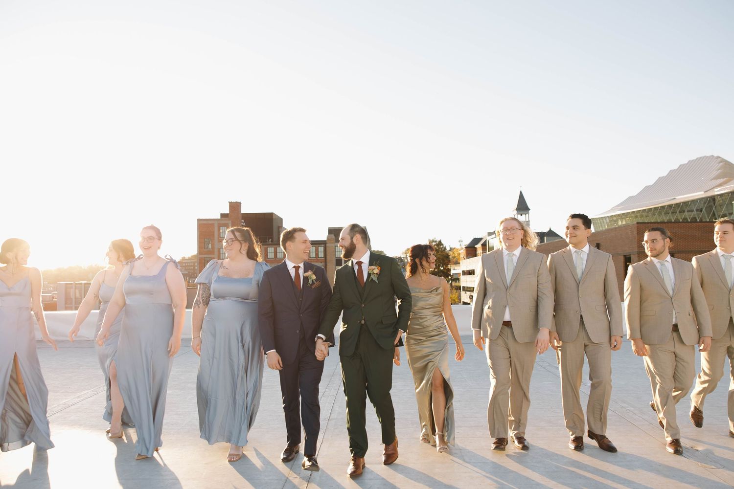Wedding party lined up against sunset sky creating silhouettes in soft golden light at outdoor ceremony.