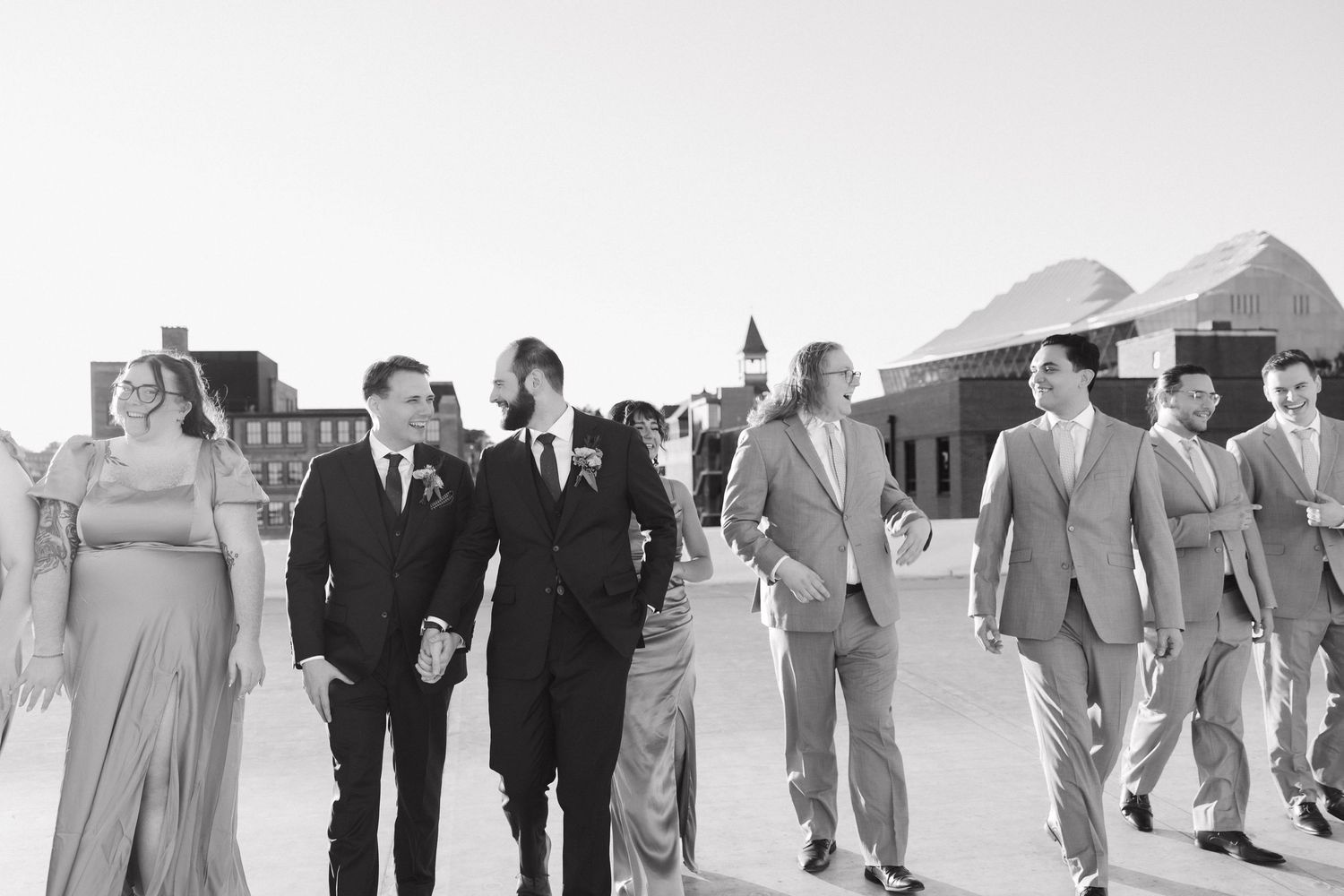 Wedding party walking in a line across a grassy field with tents visible in the background.