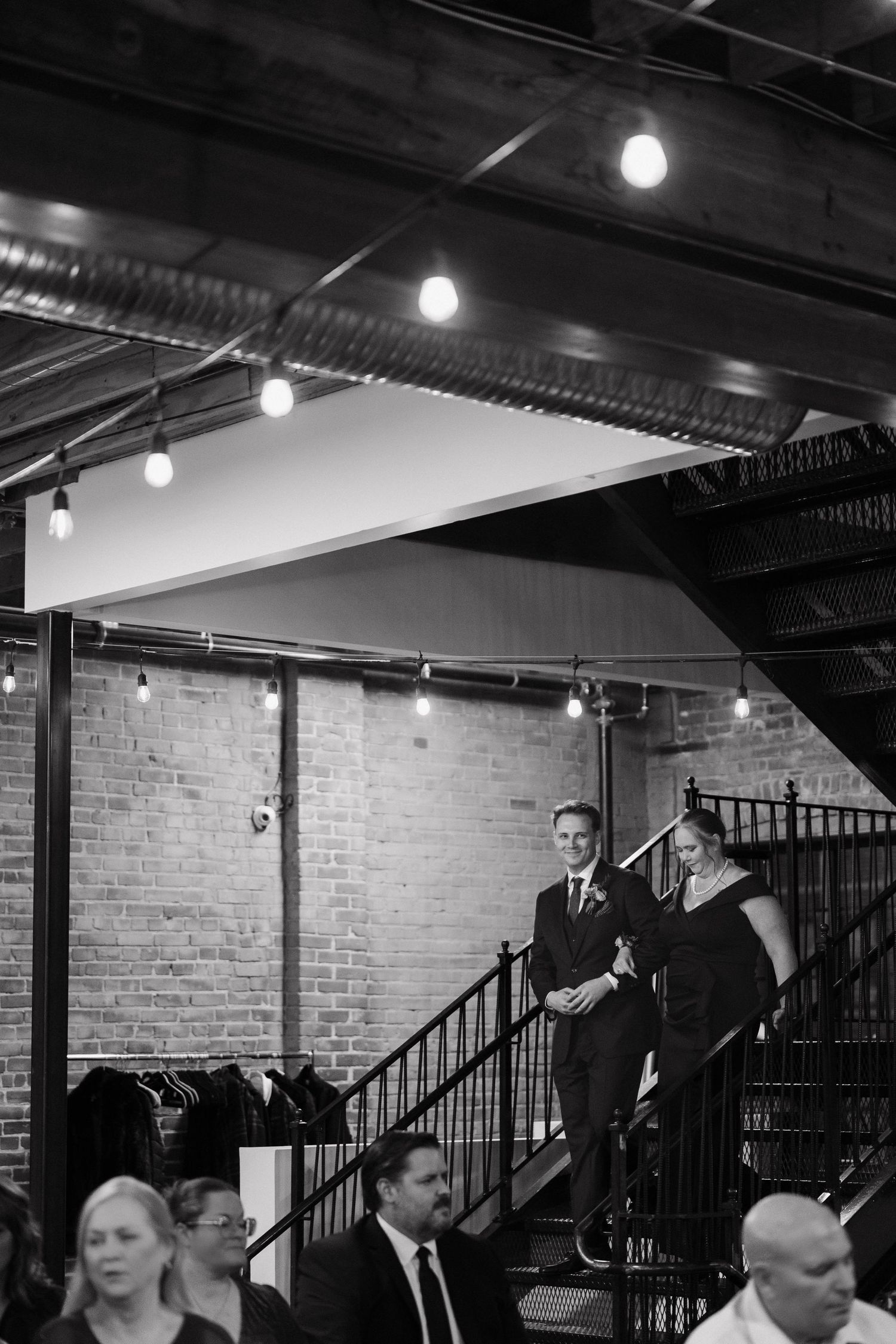 Wedding party members gather in an industrial venue with exposed brick walls and overhead lighting.