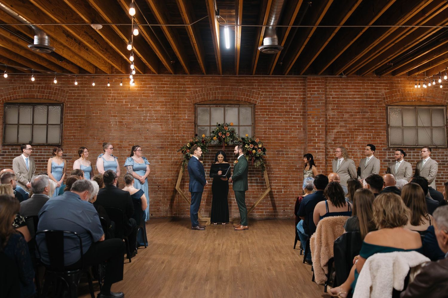 Wedding reception venue with exposed brick walls and wooden ceiling beams illuminated by string lights.