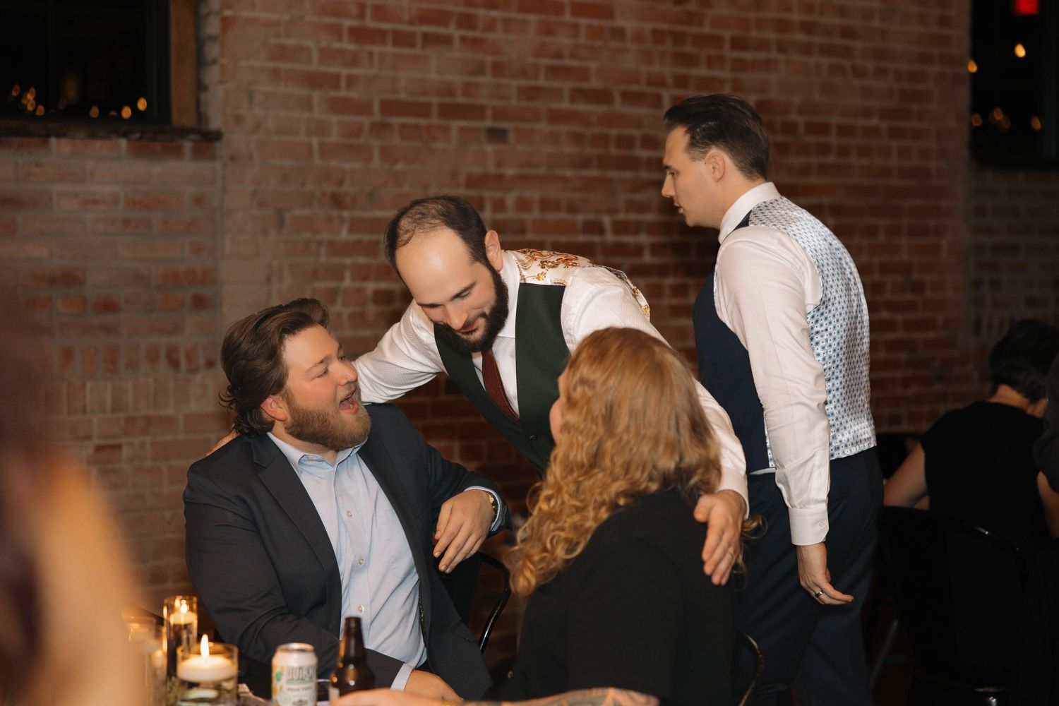 Wedding reception guests mingle and socialize in a dimly lit brick-walled venue.