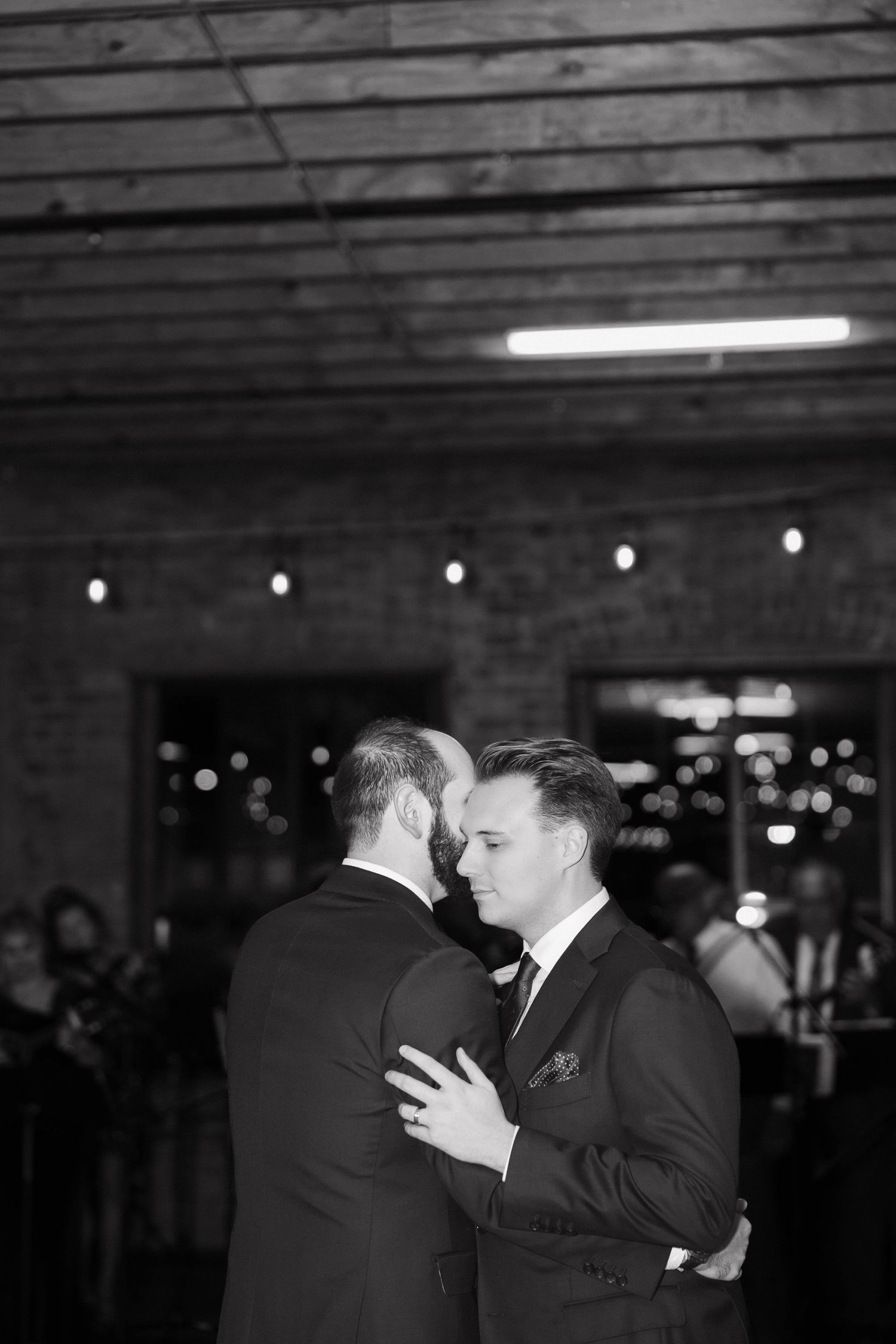 Four black and white images show couples dancing in a dimly lit ballroom setting with twinkle lights in the background.