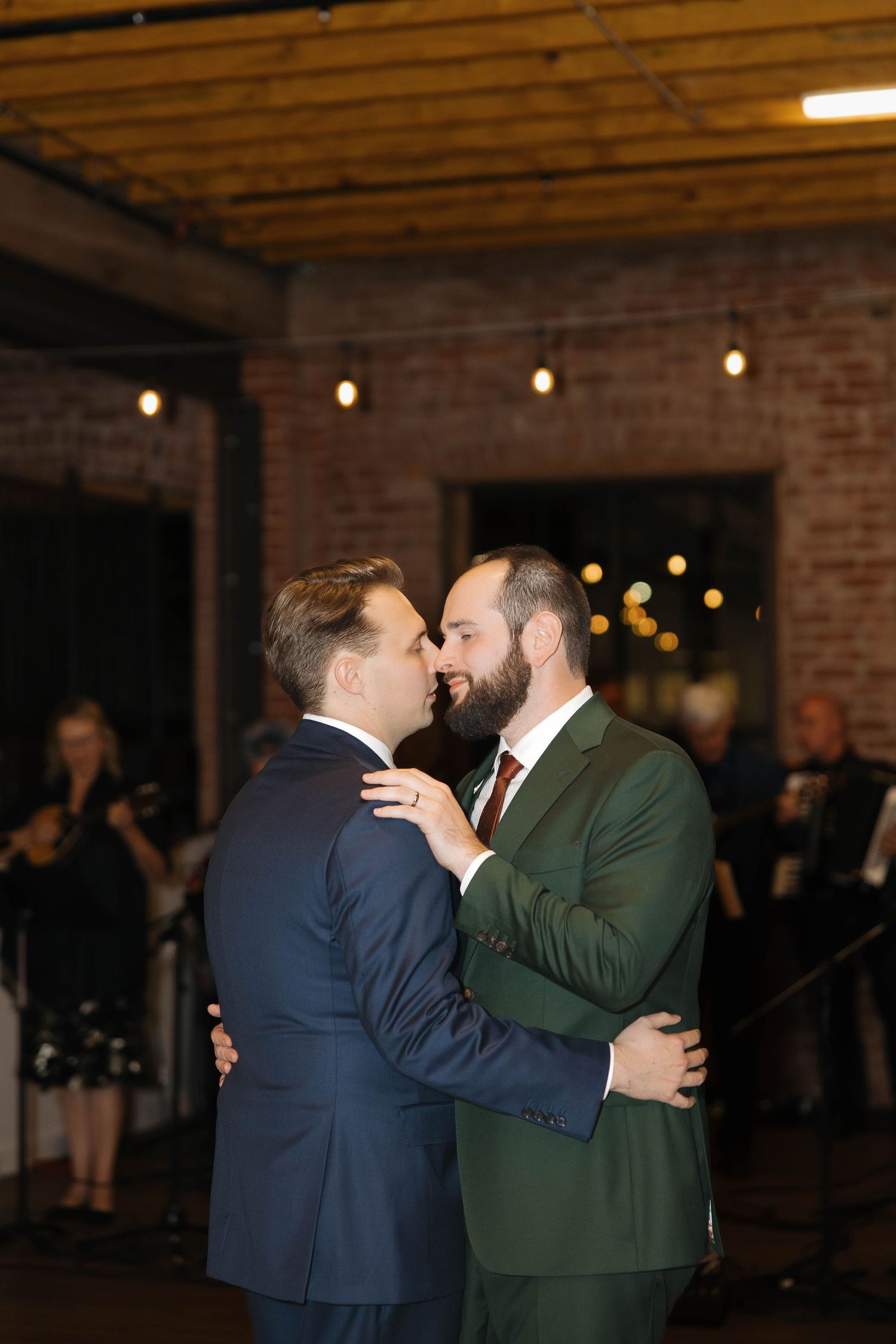 Couple sharing a romantic dance moment in a rustic venue with string lights and brick walls.