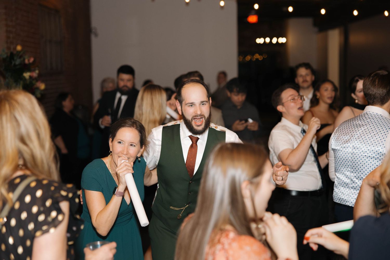 People dancing and mingling at an evening wedding reception with string lights overhead.