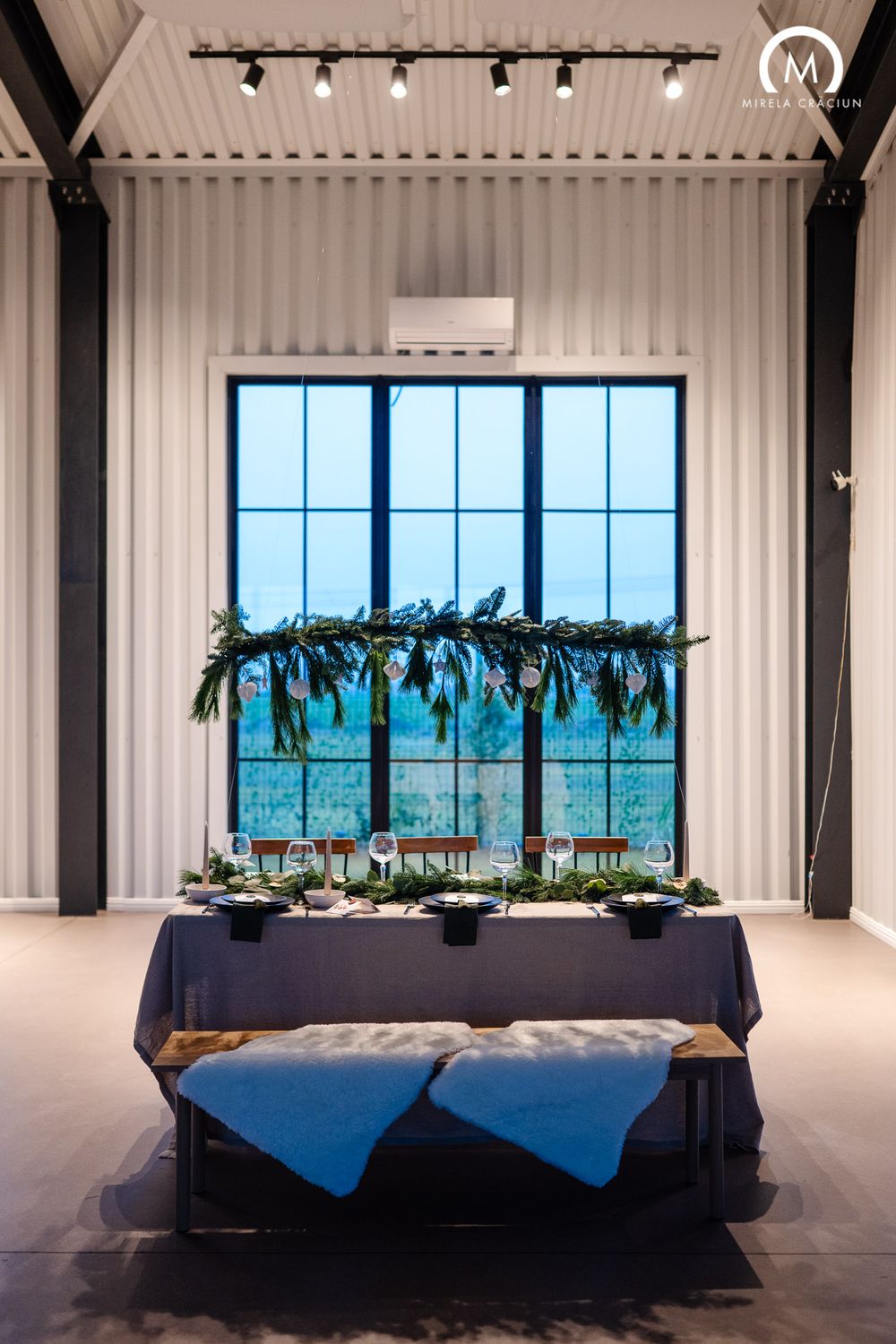 Modern event space with black curtains, white walls, and elegant table settings arranged in a row with ocean views.