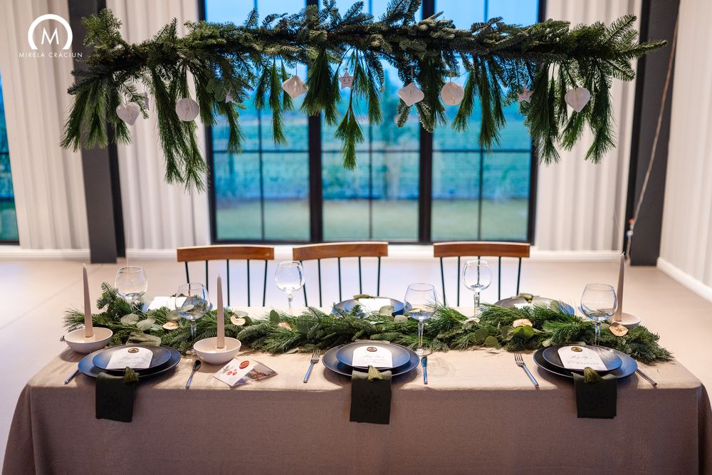 Elegant wedding reception table settings with white linens, greenery garlands, and candlelight in a bright banquet space.