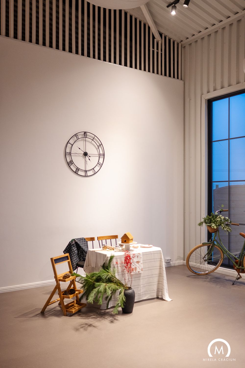 Panoramic view of a minimalist white studio space with wooden chairs, windows, and a wall clock in natural lighting.