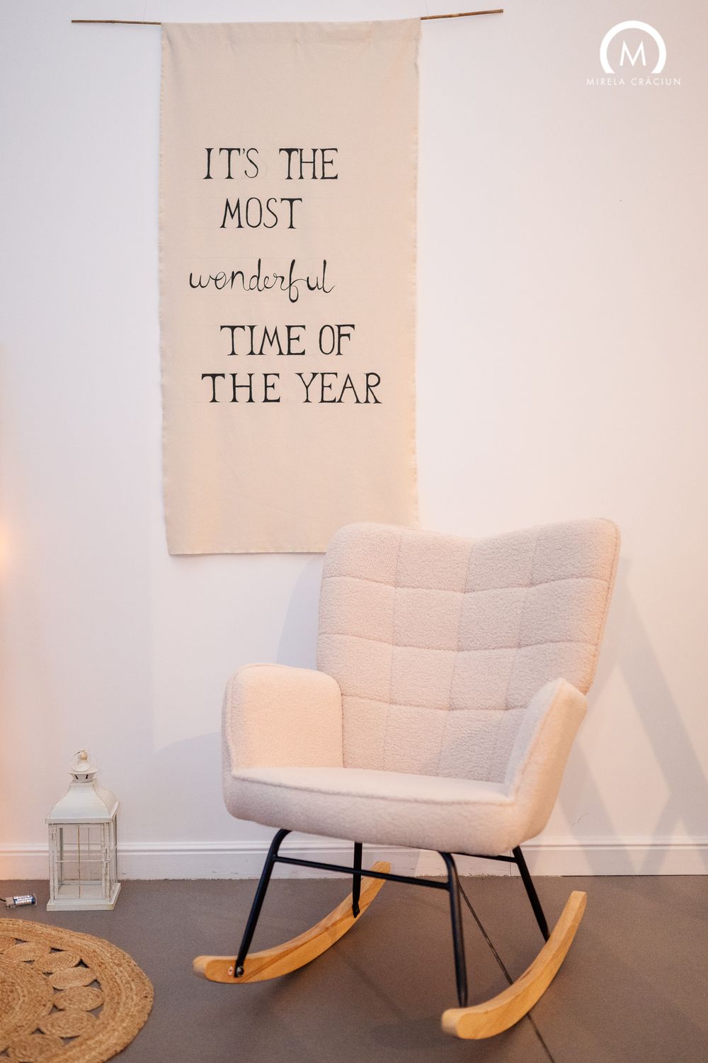 Modern rocking chair with beige upholstery sits beneath a wall hanging with 'It's the most wonderful time of the year' text.