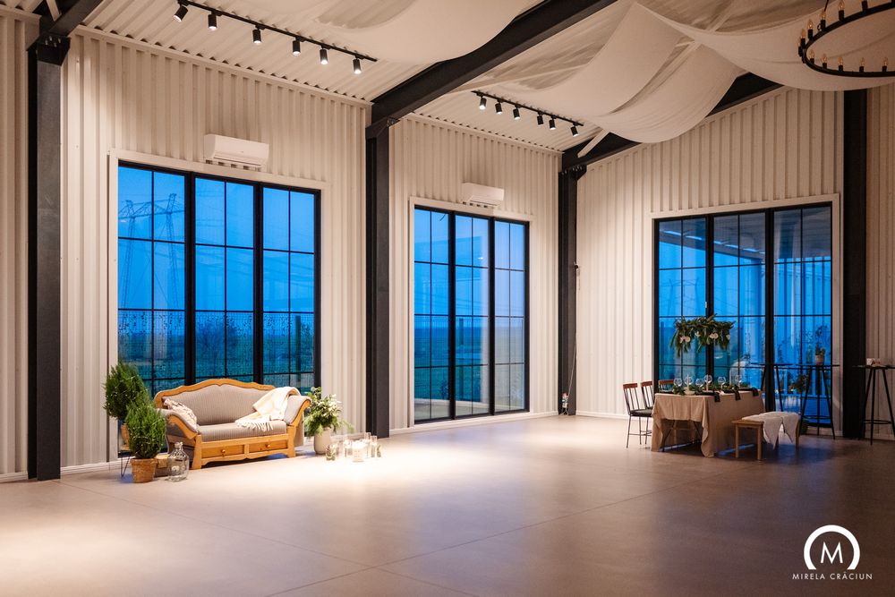 Modern event space with large windows, track lighting, and white walls in a panoramic view.