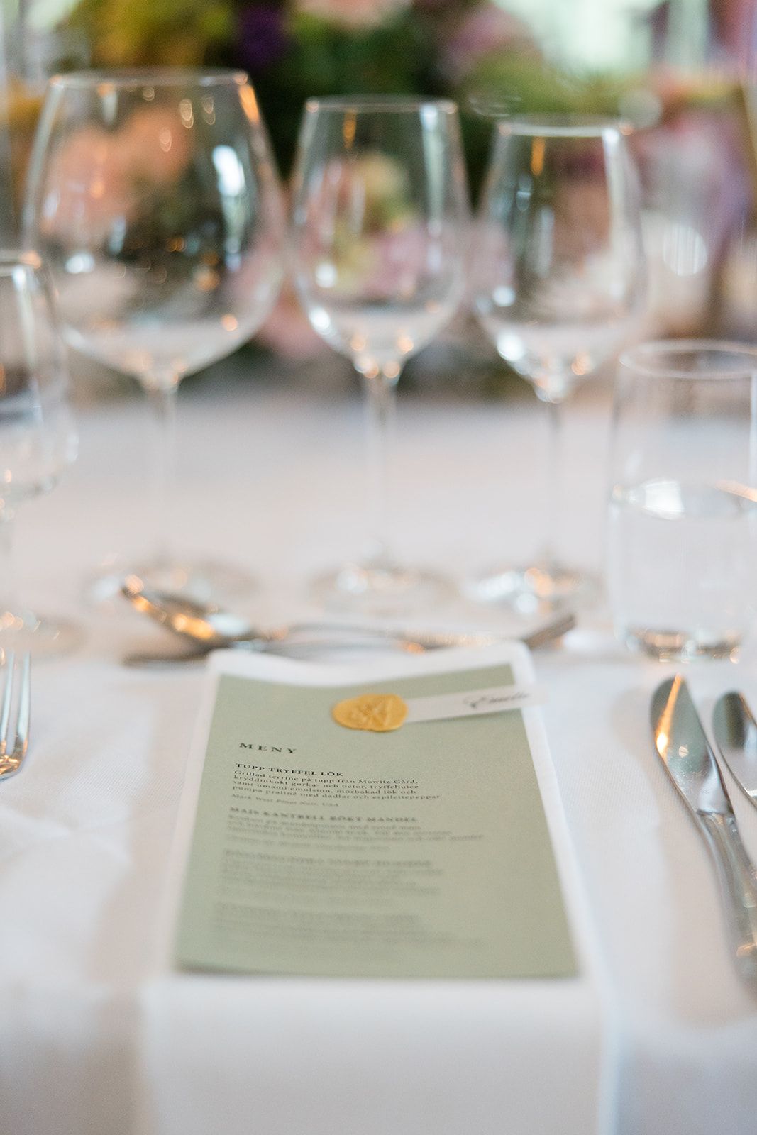 Elegant table setting at a formal event with wine glasses and printed menus on white tablecloth.