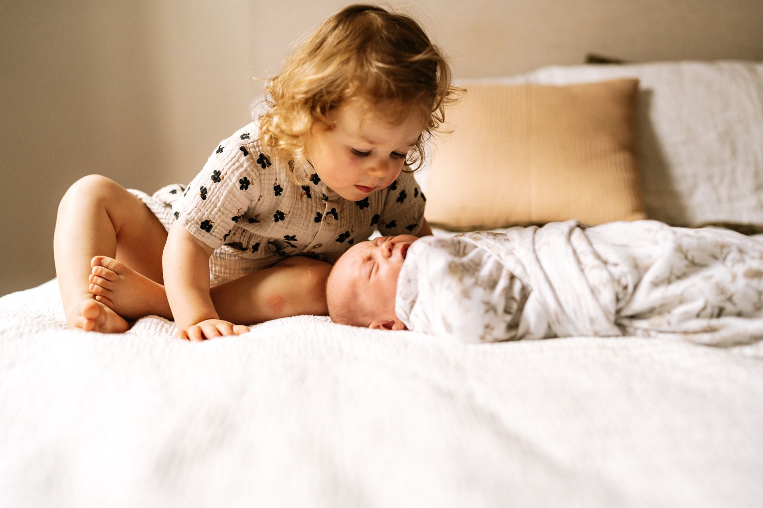 A toddler and newborn baby on a bed during an indoor newborn photography session in Perth with soft warm light