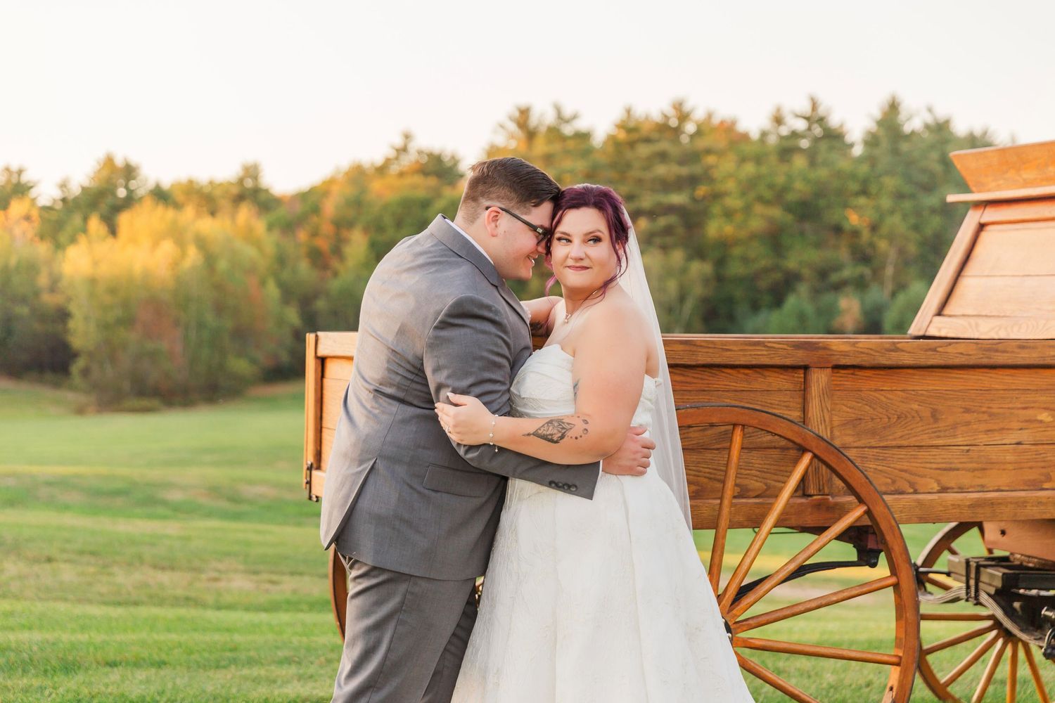 A romantic couple shares tender moments in a rustic outdoor setting with wooden wagons and autumn foliage.
