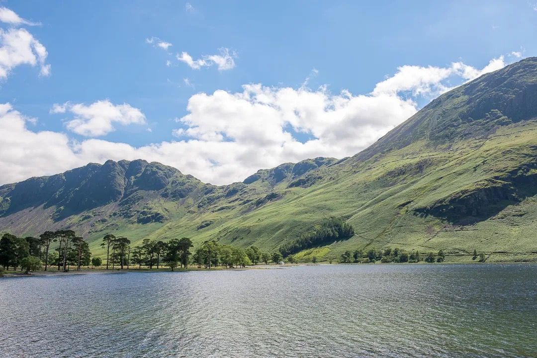 Clear lake with green mountains and blue sky behind on a sunny day.