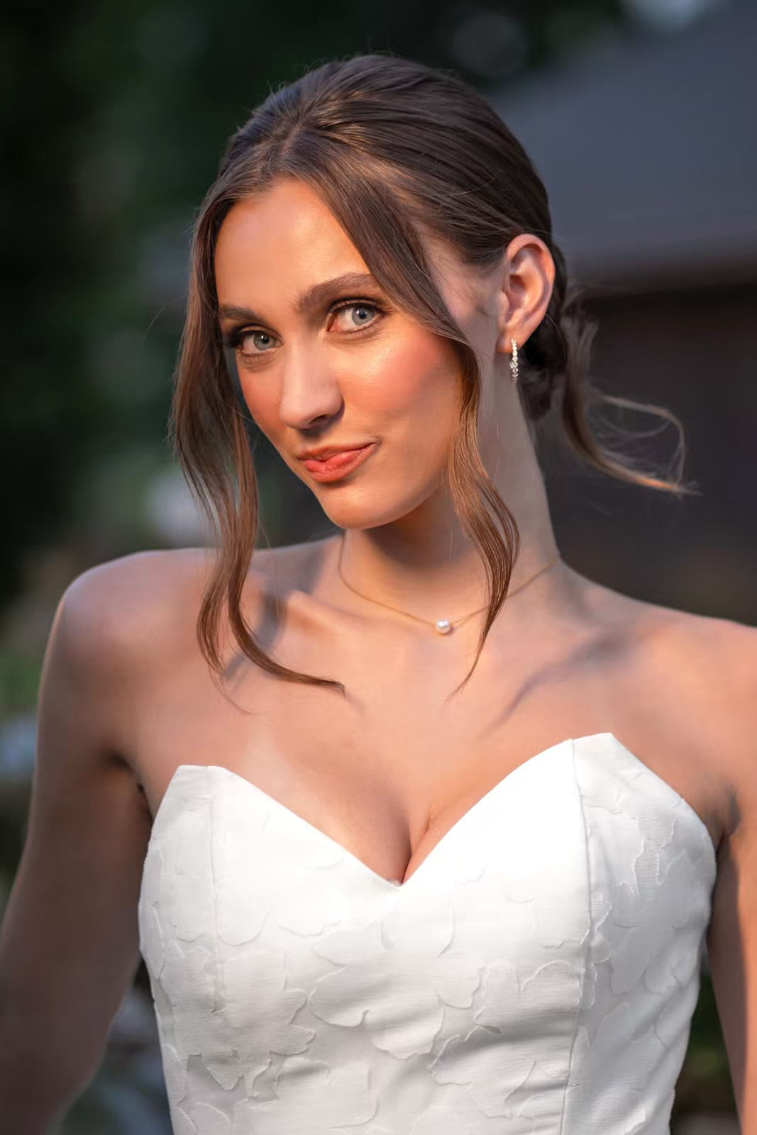 A bride in a wedding dress poses outdoors with soft lighting and natural backdrop.