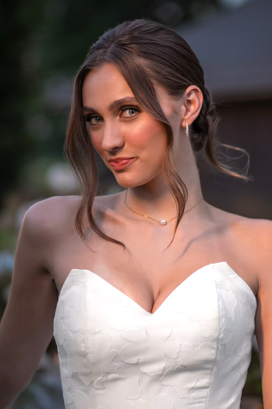 A bride in her wedding dress smiles while looking to the side in an outdoor venue.