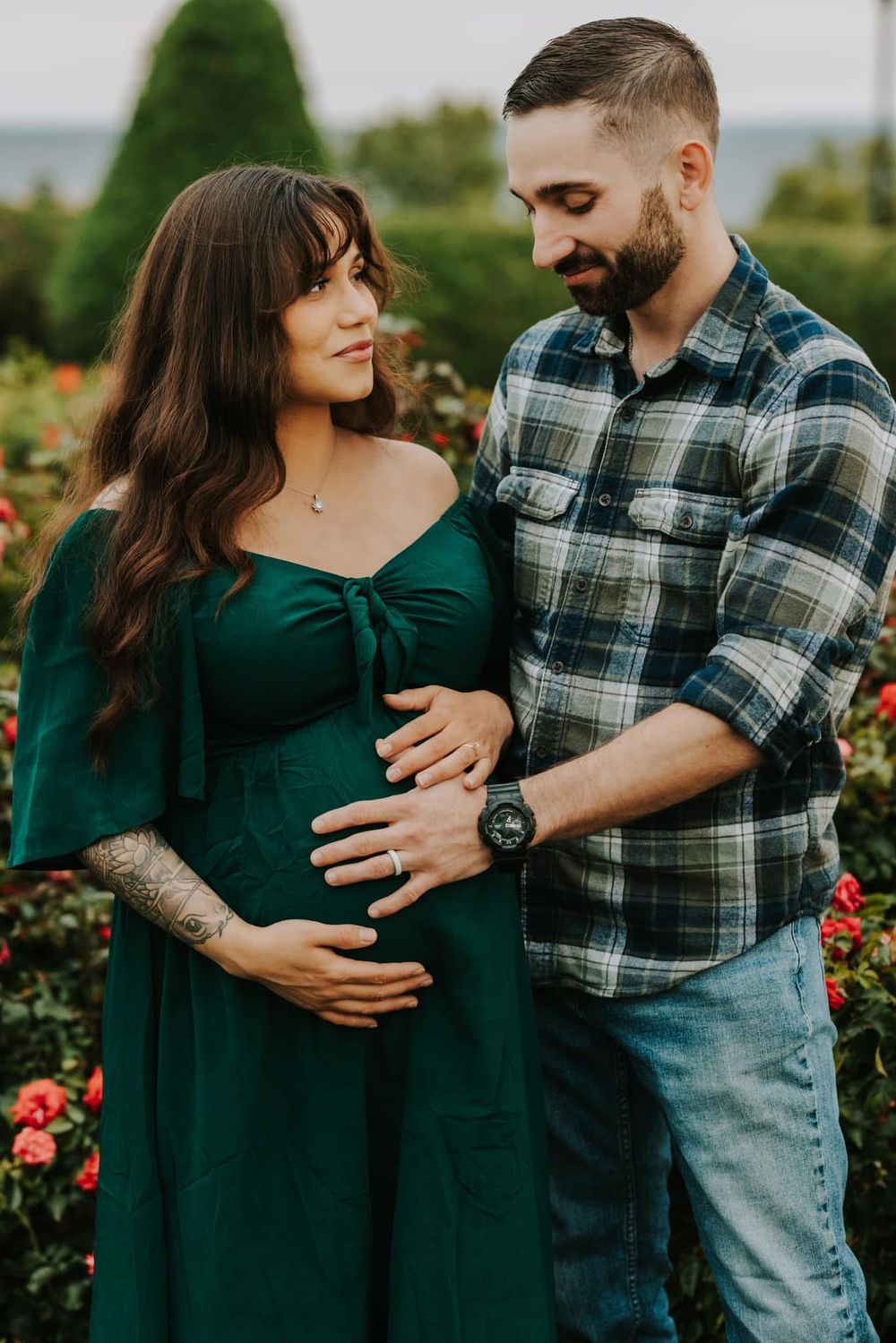 Couple shares intimate moment in garden with roses as woman in emerald dress embraces growing baby bump.